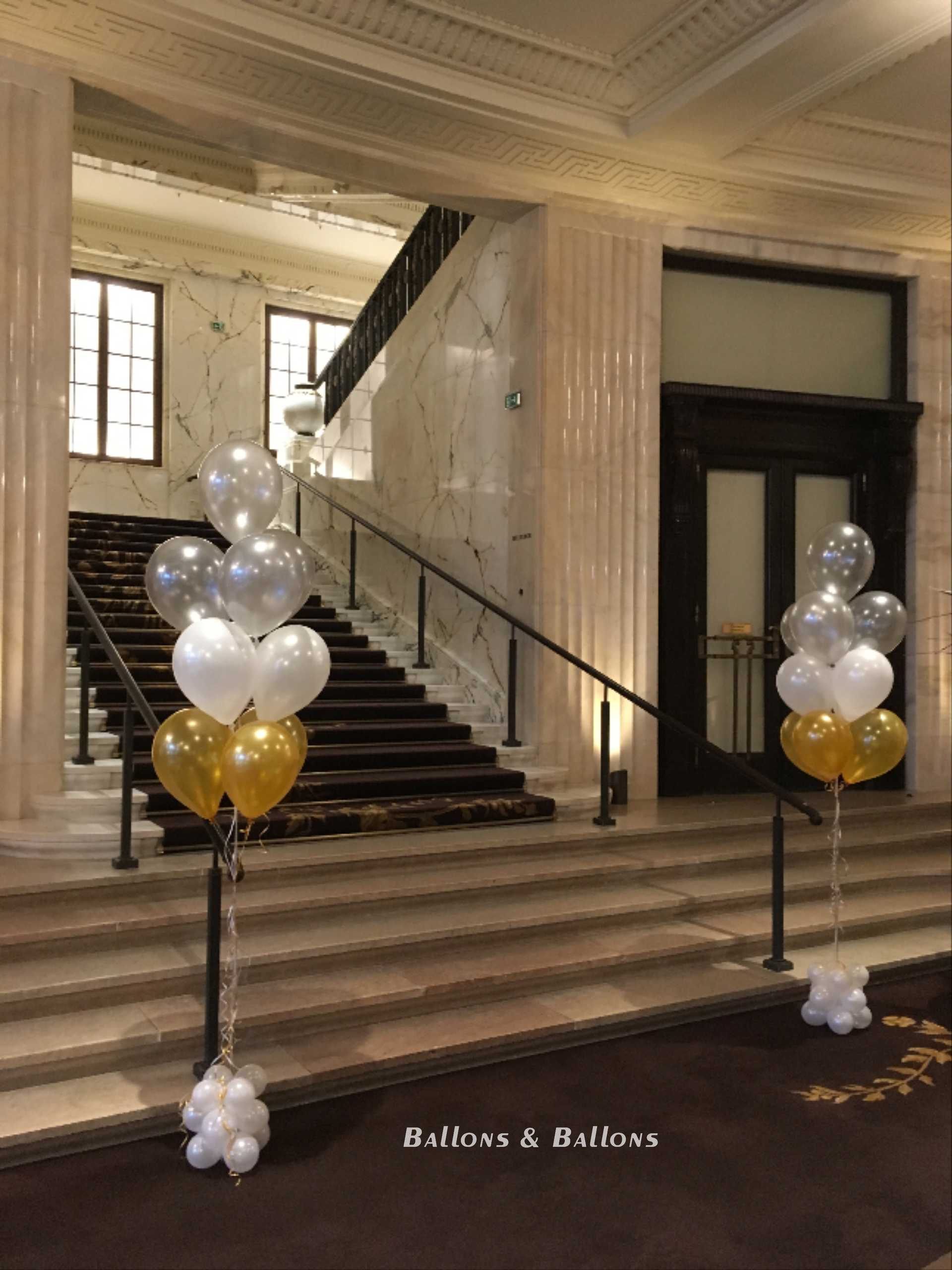 Zwei hohe goldene und weiße Ballons vor einer eleganten Treppe in Wien.