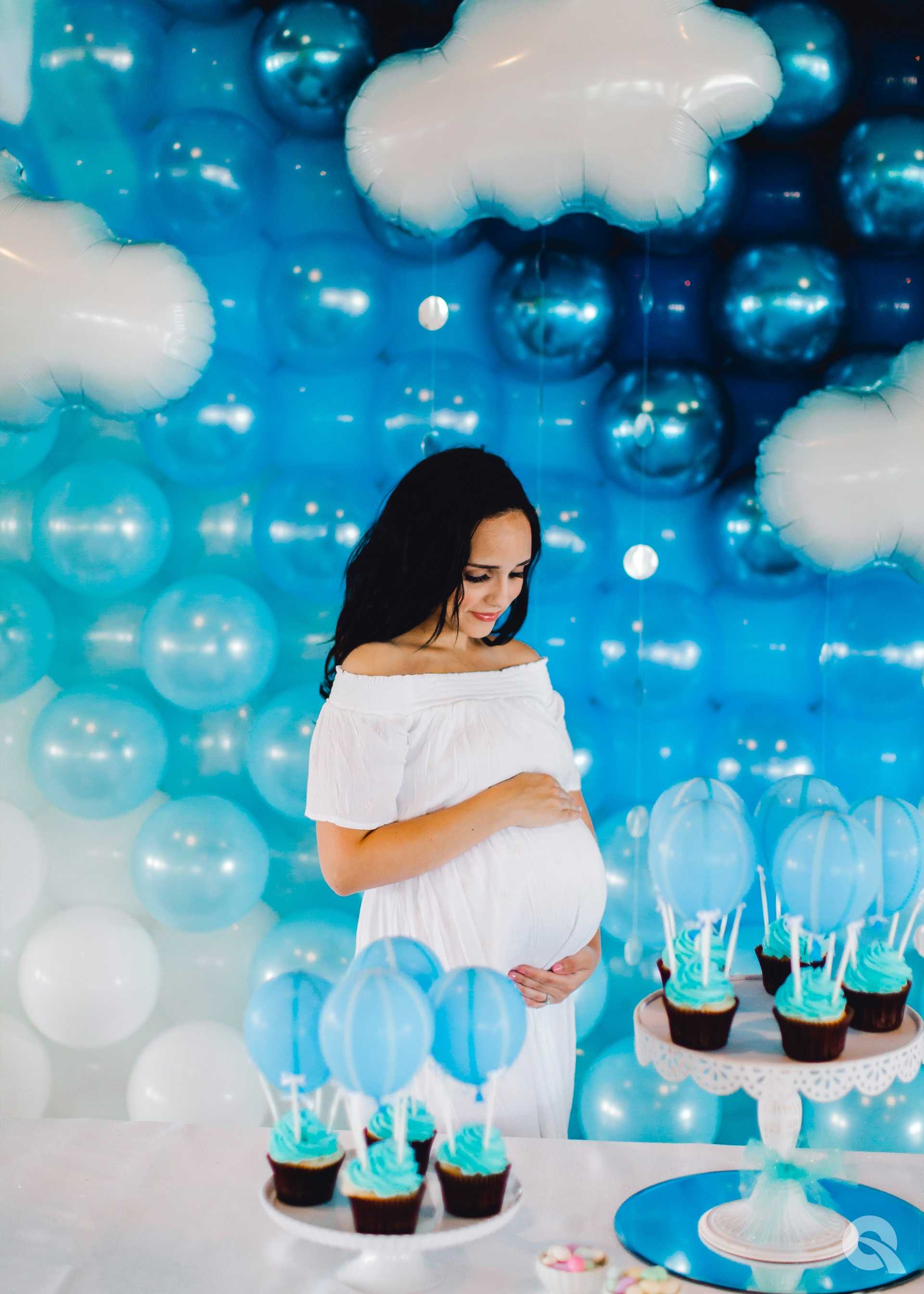 Eine schwangere Frau steht vor einem Tisch mit Cupcakes und Ballons.