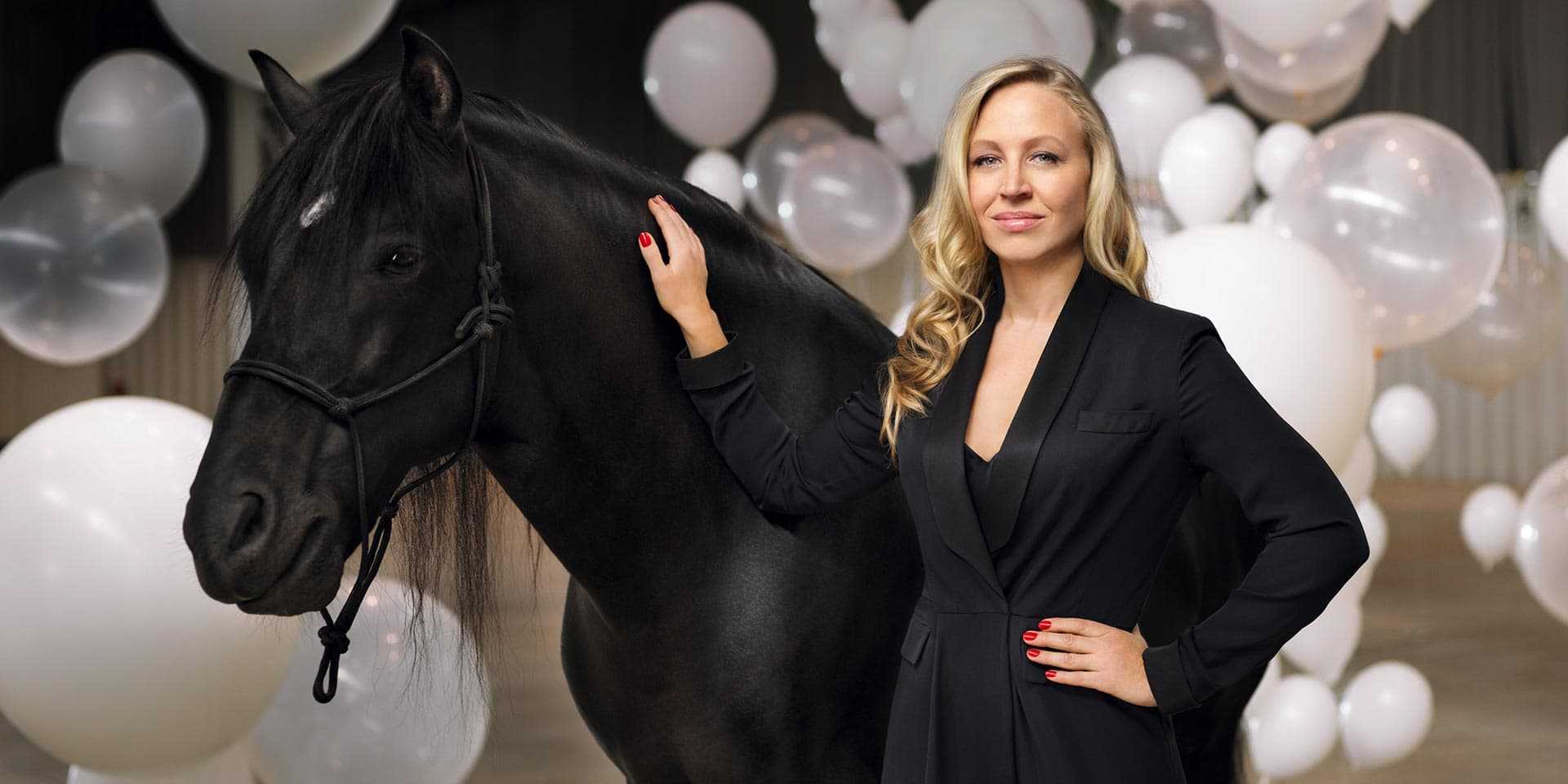 Eine Frau steht neben einem schwarzen Pferd auf einem Ball aus Ballons.