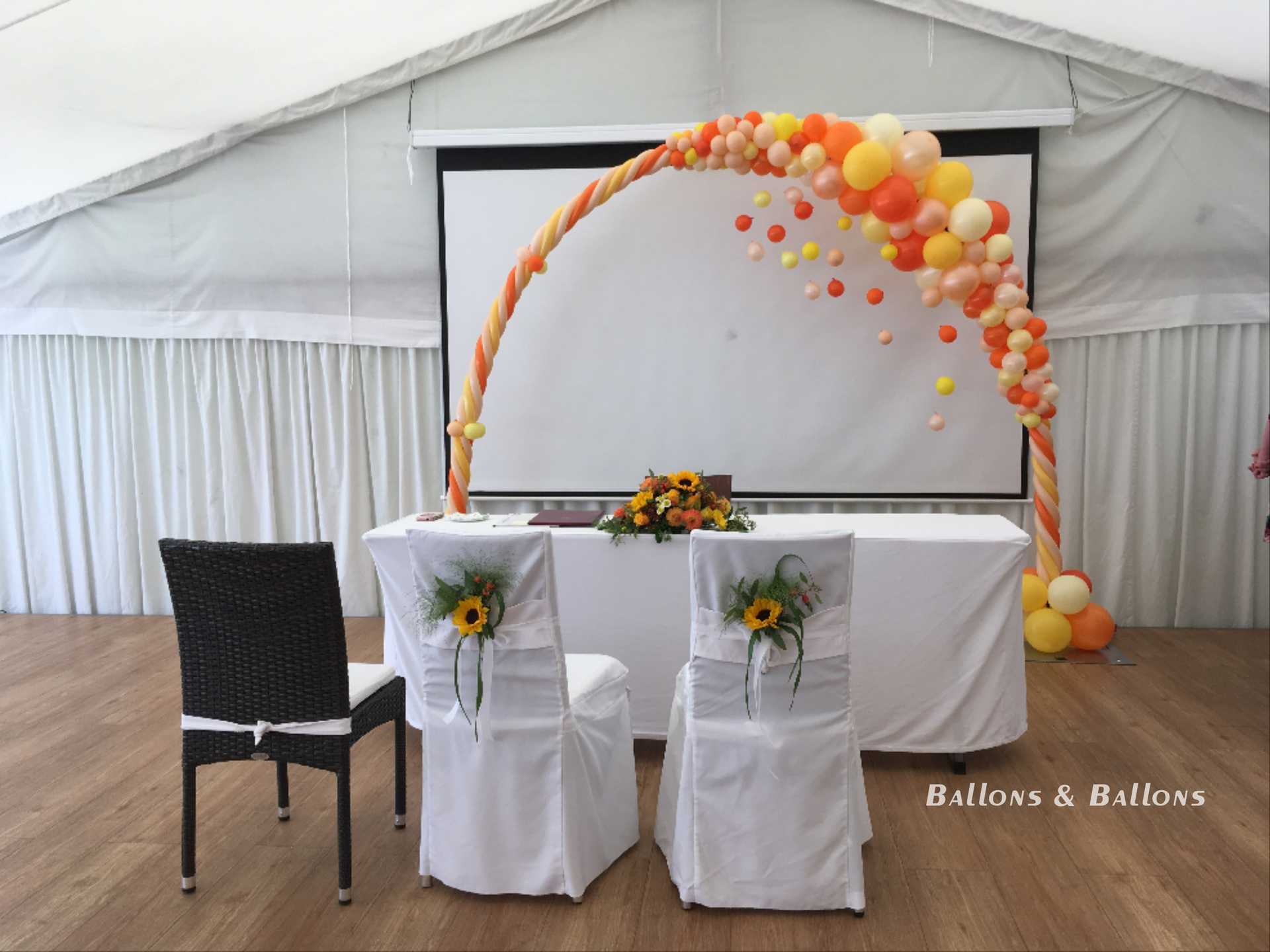Zwei Stühle neben einer Bühne mit Ballons, einem Tisch und einem Bildschirm.