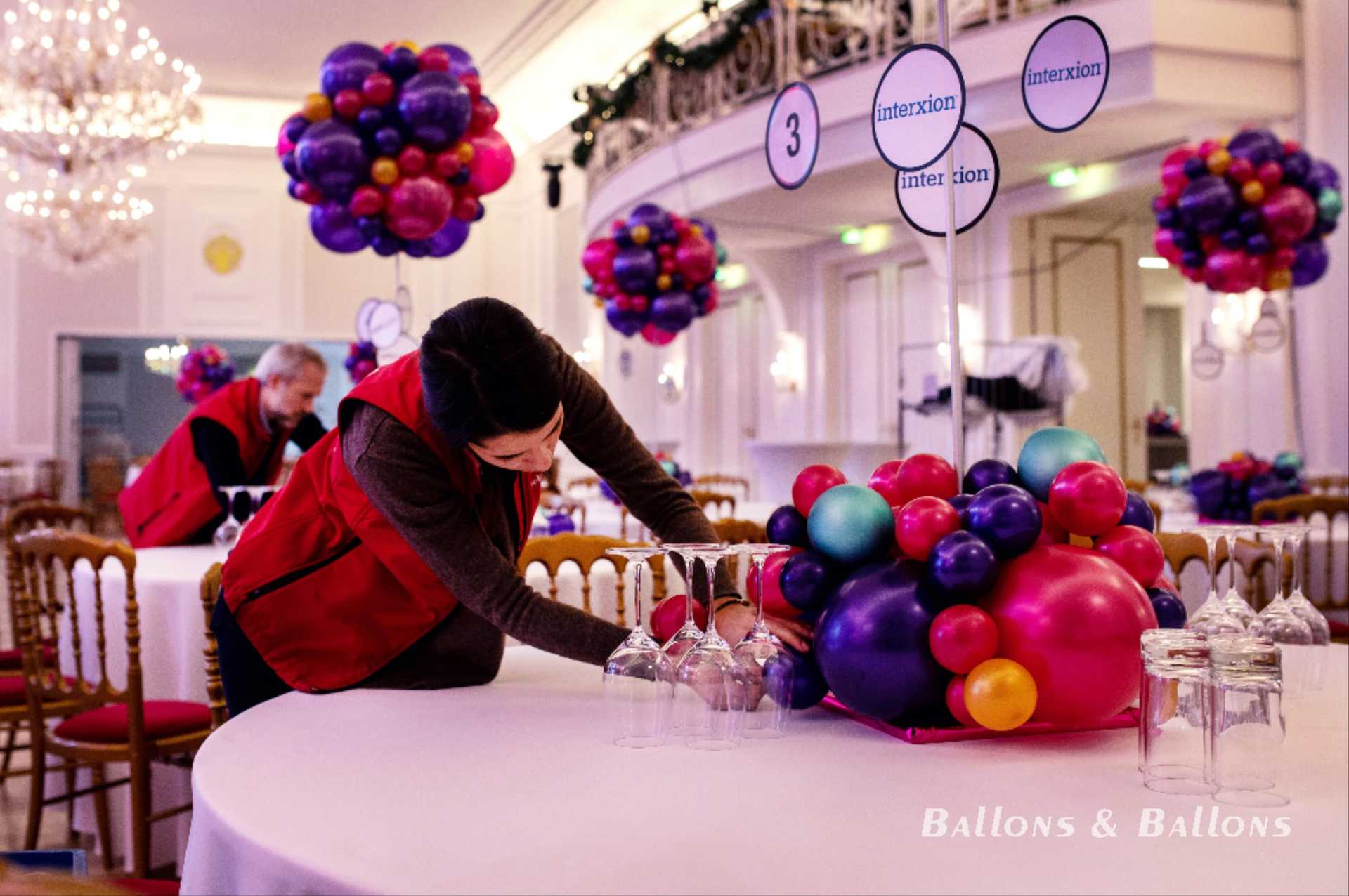 Eine Person in einem roten Jackett, die Ballons auf einem Tisch anordnet in Wien.